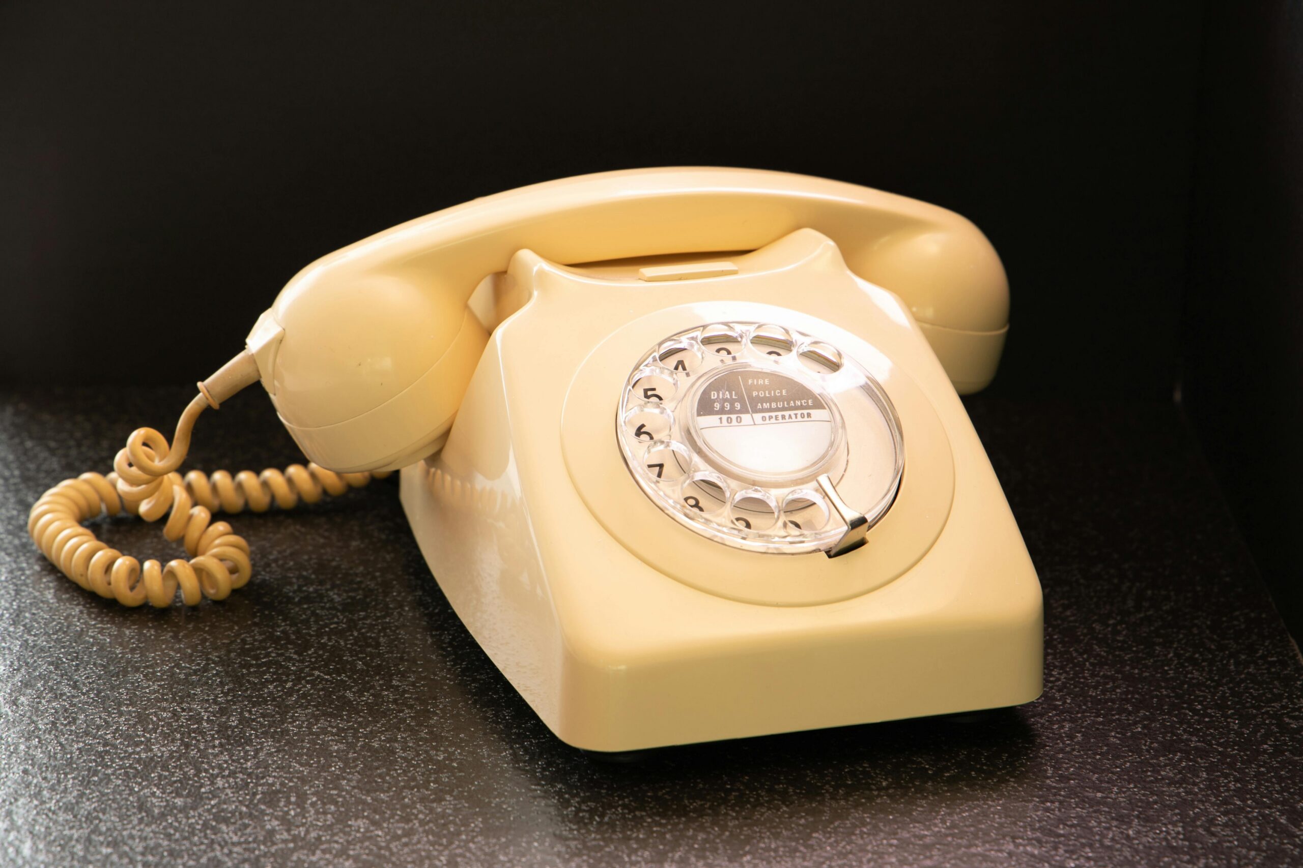 Classic beige rotary dial telephone on dark surface, evoking nostalgia and retro style.